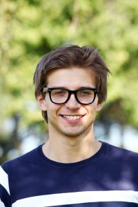 Portrait of a Progressive Learning Academy tutor wearing glasses and a striped shirt, smiling in a professional headshot with a neutral background.